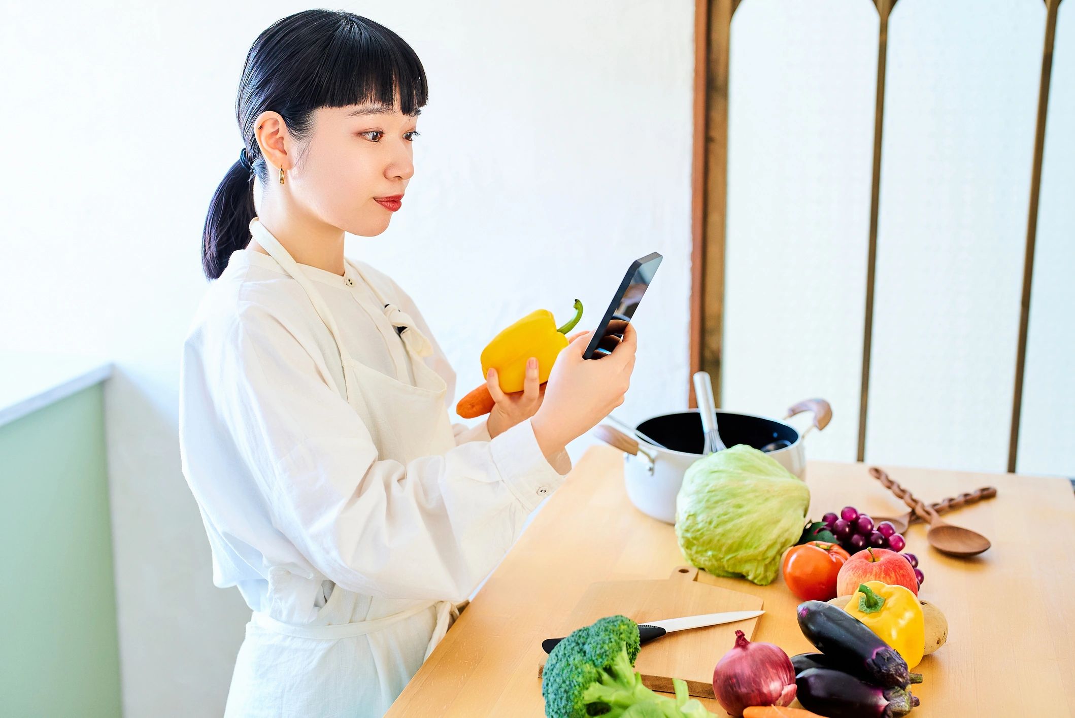 Young woman picking up vegetables and smartphone in the market.